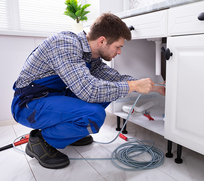A plumber in overalls repairing a sink in a kitchen.
