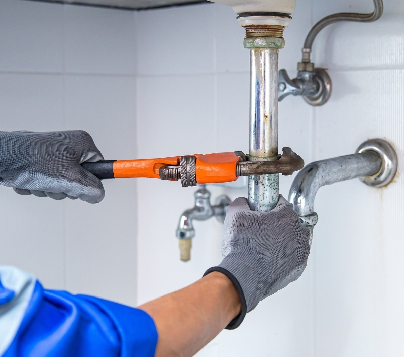 Plumber repairing a leaking pipe under an Odessa home sink